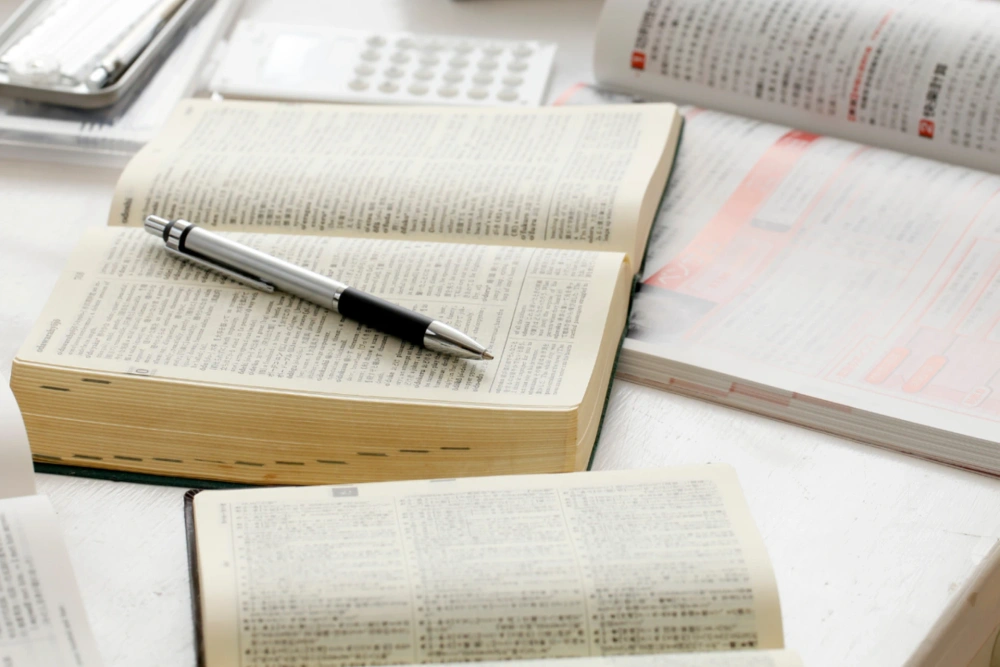 開いた専門書の上にペンが置かれ、周りにも資料が広げられてエビデンスを重視していることを示している写真