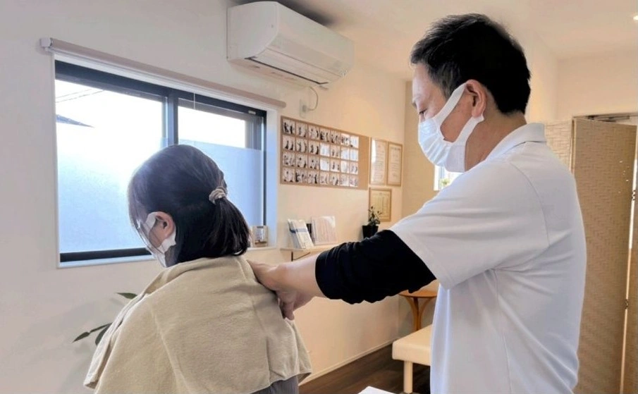 院長がベットに座った女性の肩に手を当て、施術をしている風景