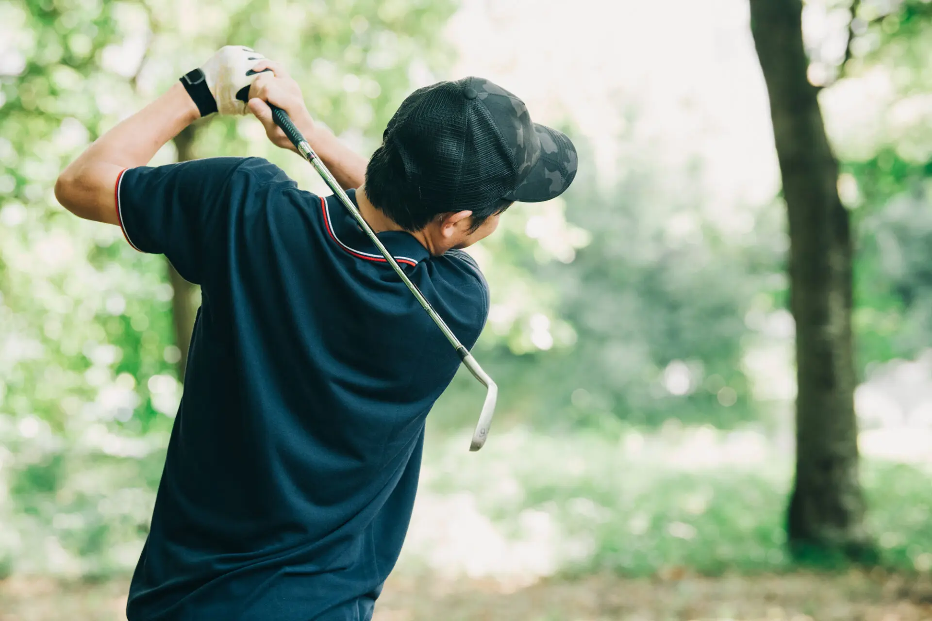 木々を背景に、ゴルフクラブを振り抜いた男性を後ろから撮った写真
